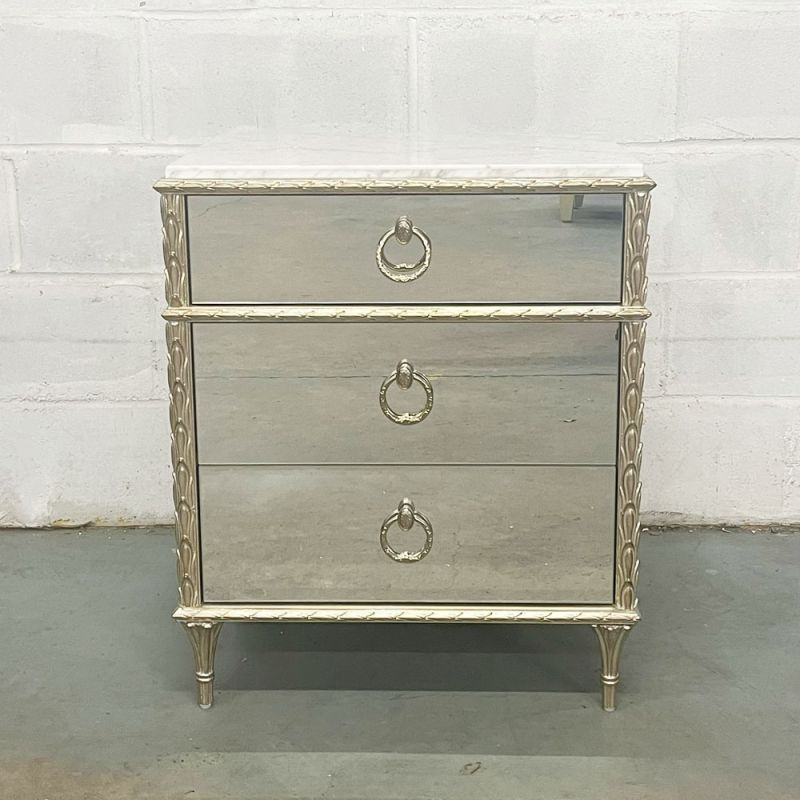 A mirrored bedside table with three drawers and a marble top 