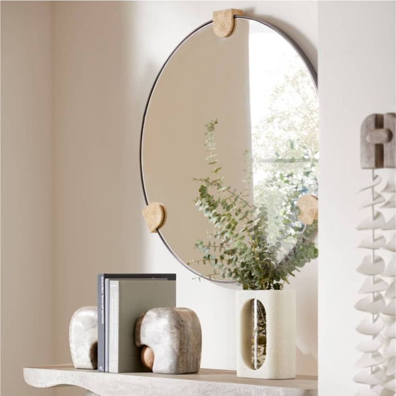 The Clasp Wall Mirror combines faux travertine resin and bronze-plated steel, creating a striking contrast between textured warmth and smooth reflection, with subtle variations in finish.