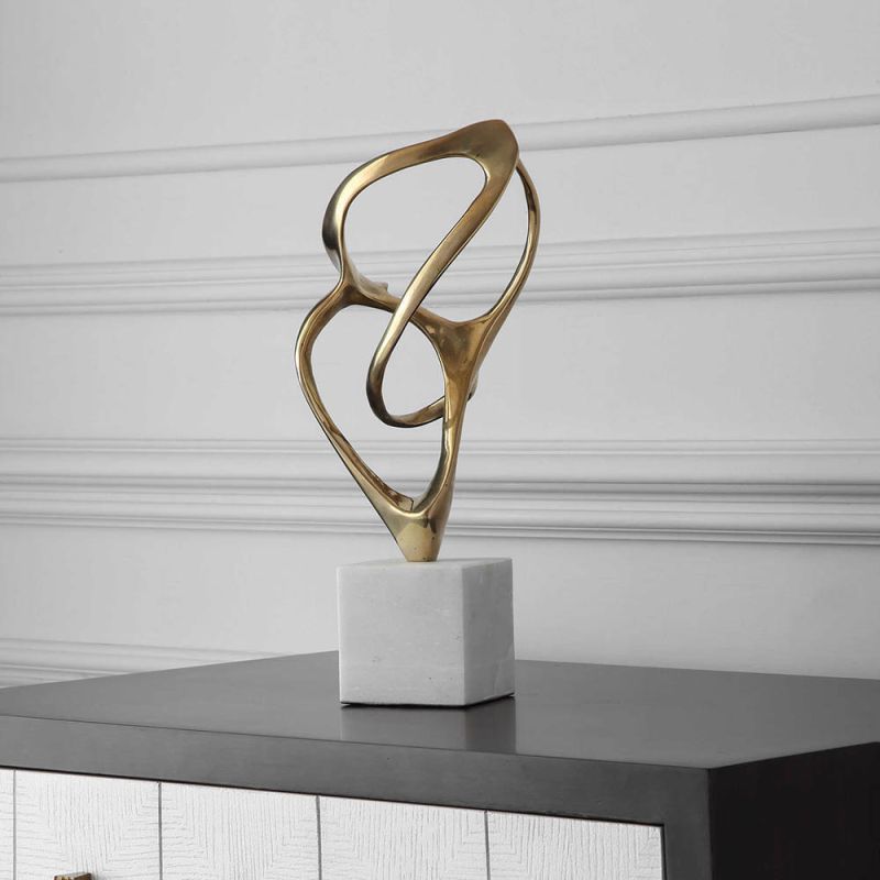 Swirling brass structure sculpture on white marble base