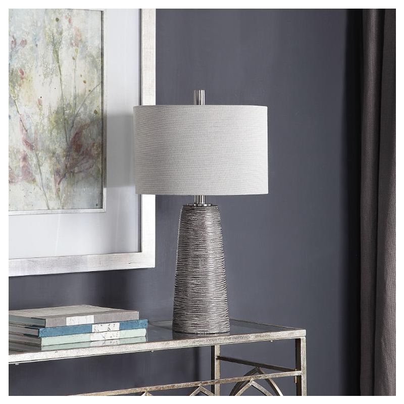 This lamp has a textured rustic bronze base with a grey wash, nickel accents, and a beige linen shade for a refined look.