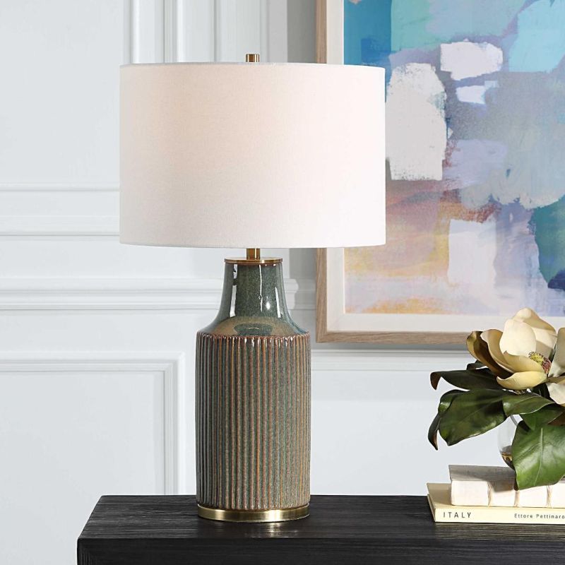 This ceramic table lamp features a bluish-green finish with rust undertones, brushed brass accents, and a white linen shade, adding sophisticated charm to any space.