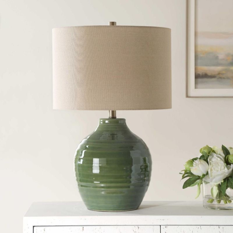 This elegant ceramic lamp has a moss green glaze, brass accents, and a beige linen shade.