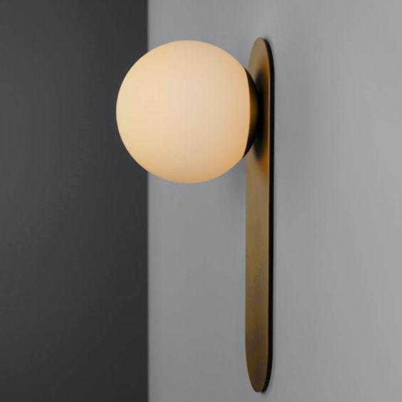 A glamorous wall lamp by Schwung with a brushed brass finish and detailed clear glass bulb