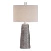 This lamp has a textured rustic bronze base with a grey wash, nickel accents, and a beige linen shade for a refined look.