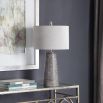 This lamp has a textured rustic bronze base with a grey wash, nickel accents, and a beige linen shade for a refined look.