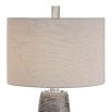 This lamp has a textured rustic bronze base with a grey wash, nickel accents, and a beige linen shade for a refined look.