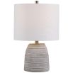 This table lamp has a concrete base with white etching, brushed nickel accents, and a light beige linen shade, offering modern sophistication and understated elegance.