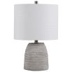 This table lamp has a concrete base with white etching, brushed nickel accents, and a light beige linen shade, offering modern sophistication and understated elegance.