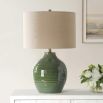 This elegant ceramic lamp has a moss green glaze, brass accents, and a beige linen shade.